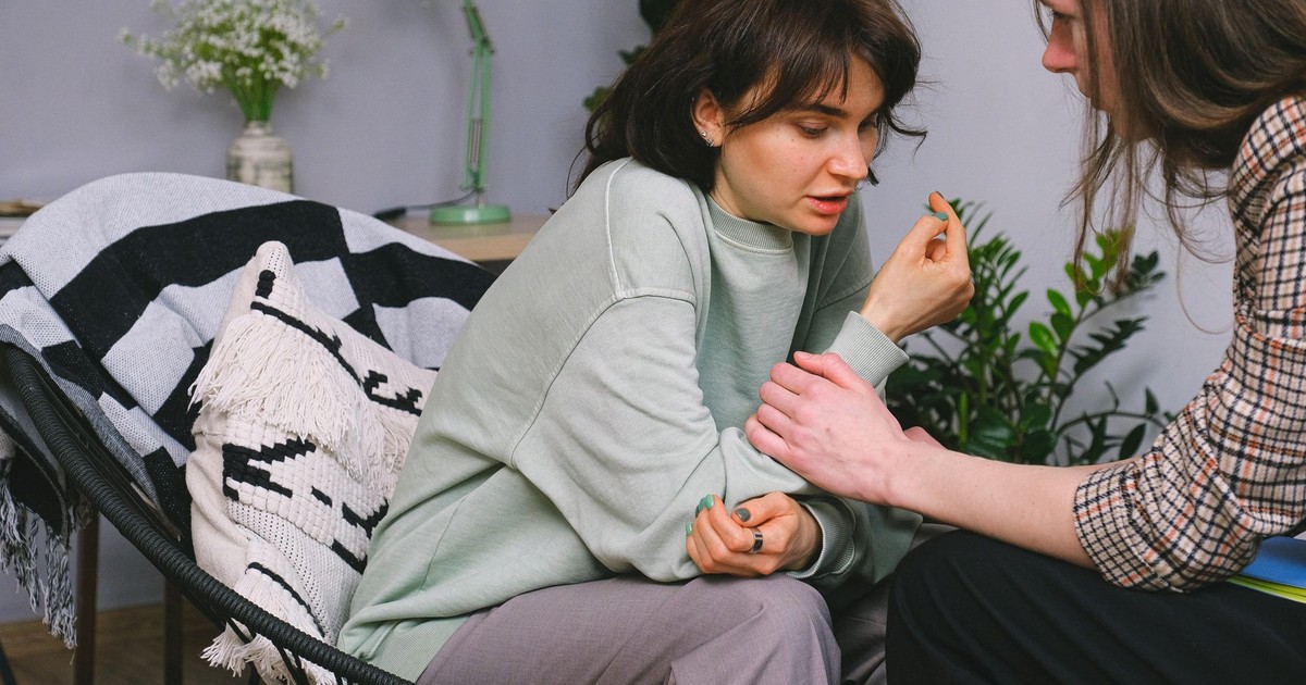 Crop psychotherapist holding adult woman by arm while talking during psychological session in light house