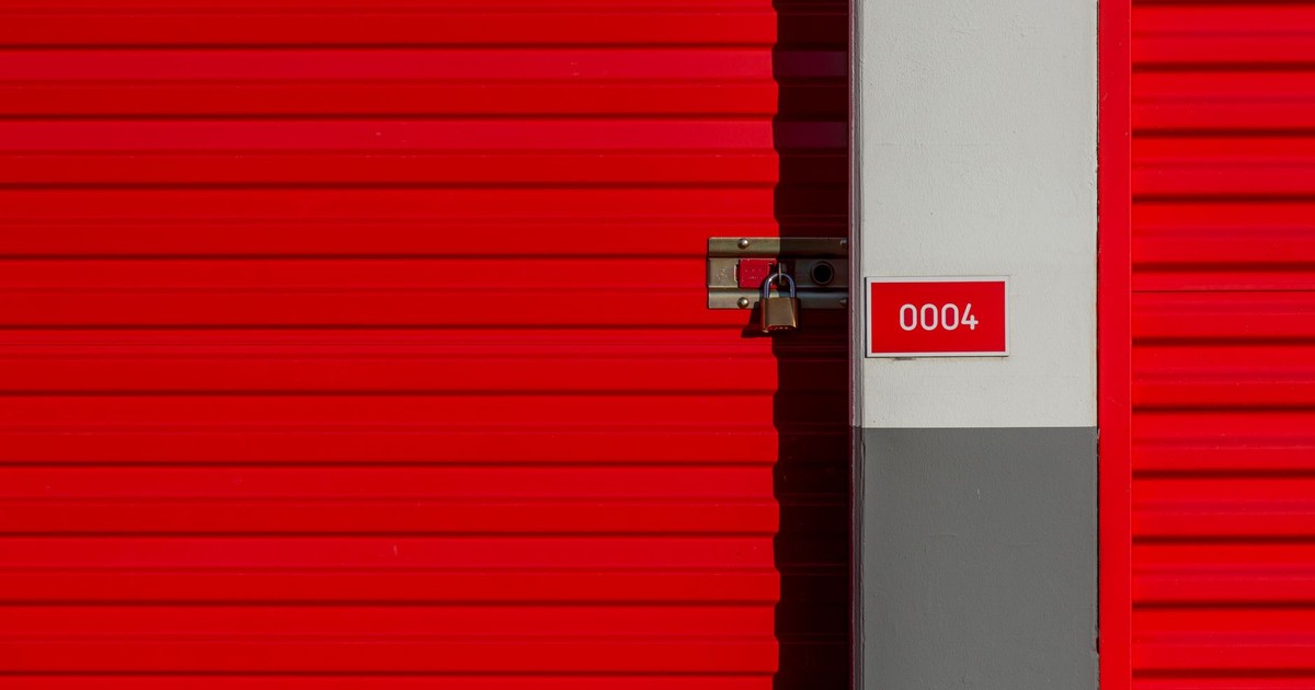 Red metal storage unit door with padlock and number 0004 sign on white panel.