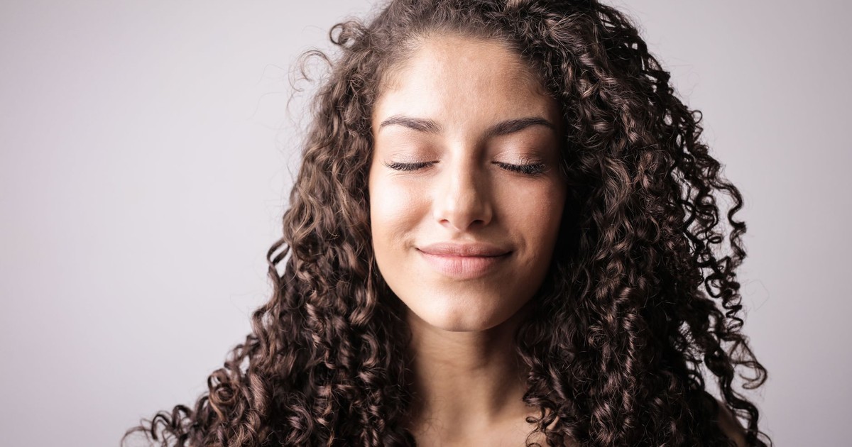 A close-up portrait of a smiling woman with curly hair, eyes closed, exuding happiness.