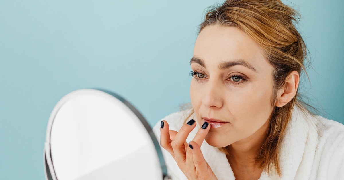 A woman in a bathrobe applies lip balm while looking in a mirror, highlighting skincare and self-care.