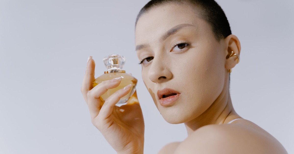 Close-up portrait of a woman with short hair holding a perfume bottle, showcasing elegance and style.