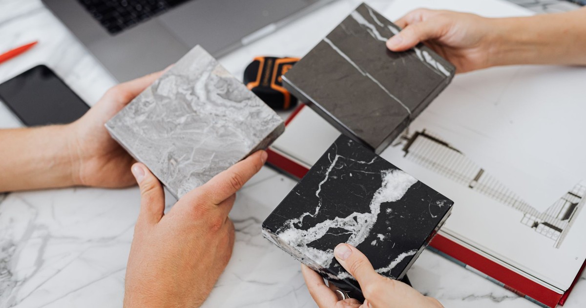 Two architects selecting marble tile samples on a desk in an office setting.