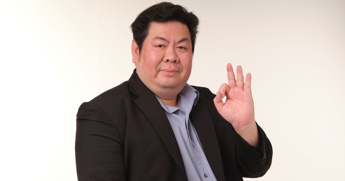 Smiling man in a suit confidently displaying the OK hand gesture.