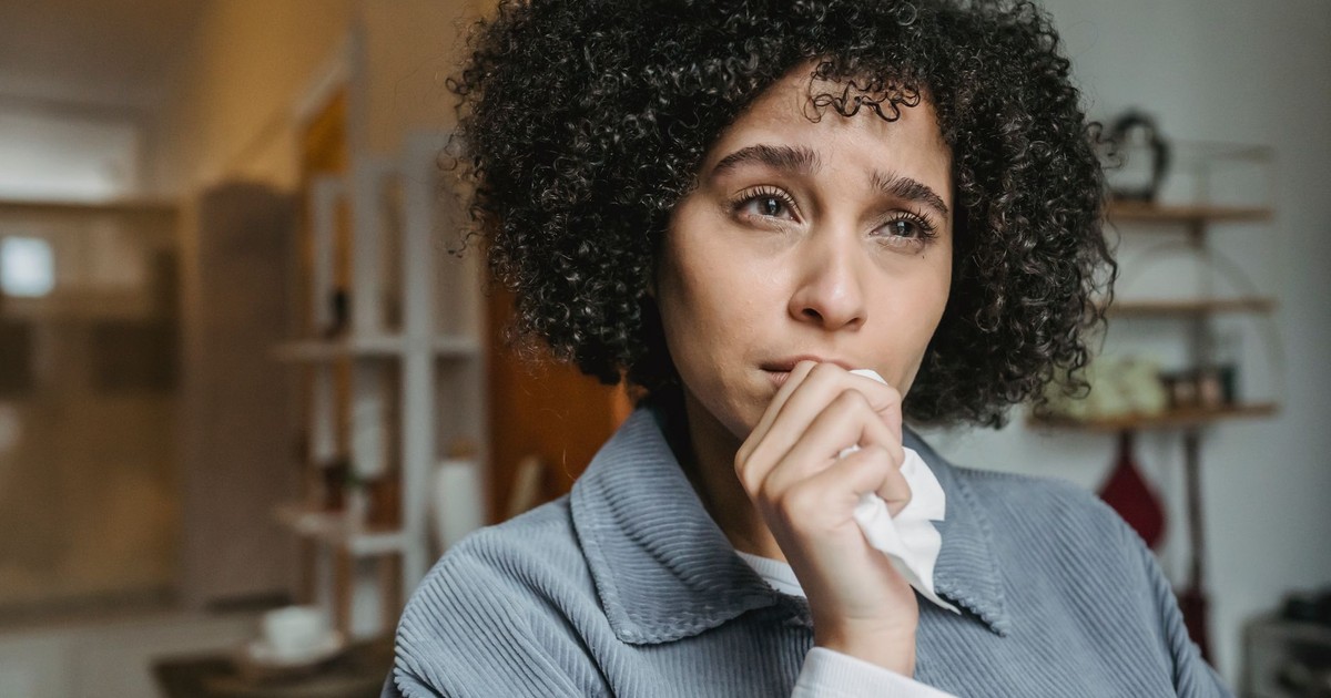 Unhappy African American woman with Afro hairstyle touching chin with tissue while looking away with sorrow