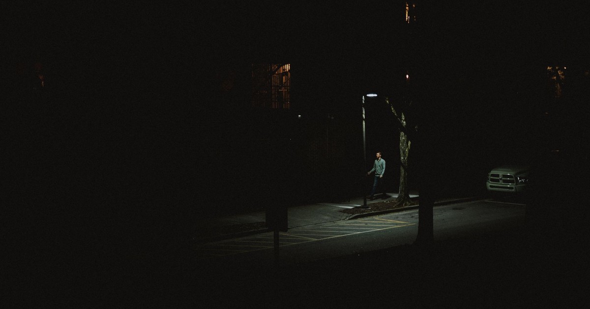 A lone person walking under a streetlight on a dark city street at night.