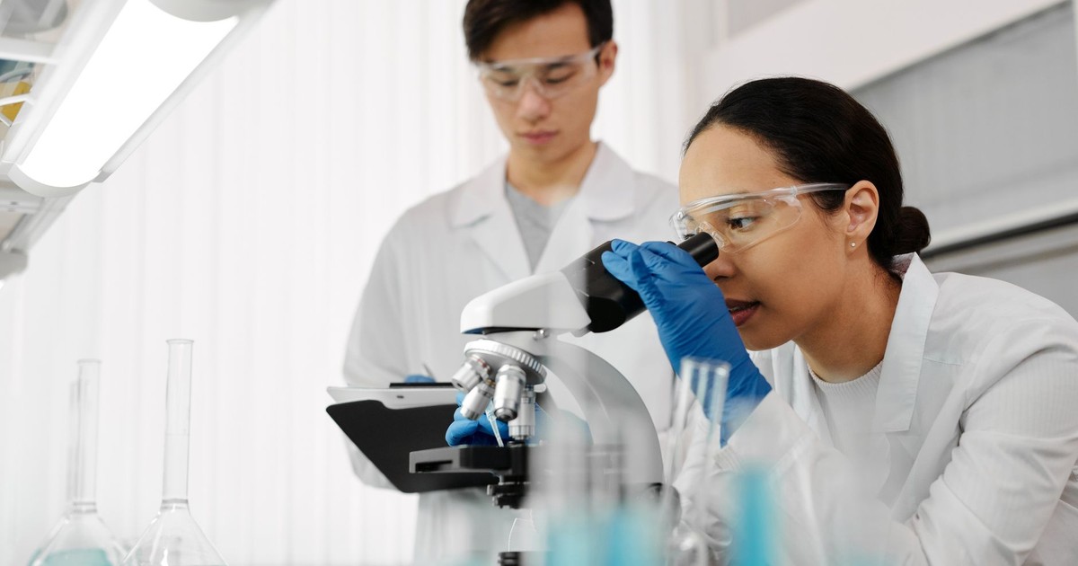 Two scientists in a laboratory using a microscope and analyzing samples.
