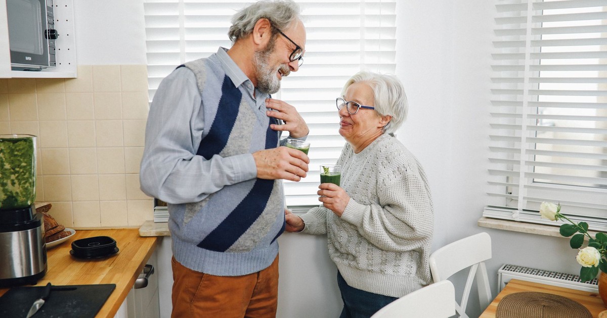 Happy senior couple enjoying refreshing green smoothies together in a cozy kitchen.