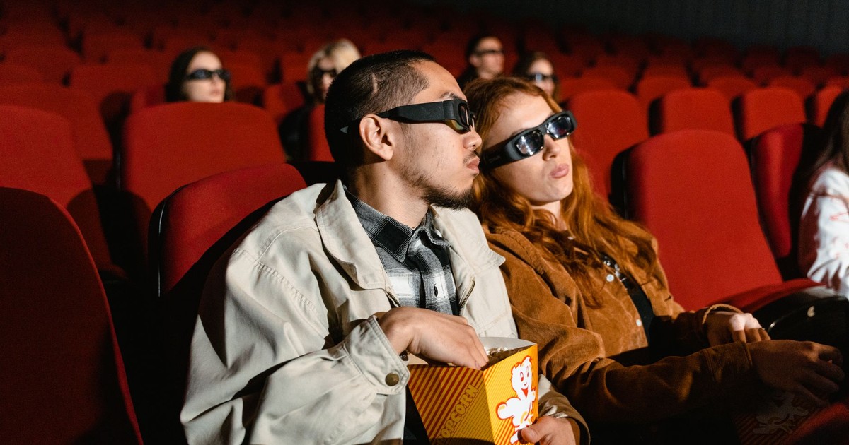 Couple wearing 3D glasses watching a movie in a cinema, enjoying popcorn.