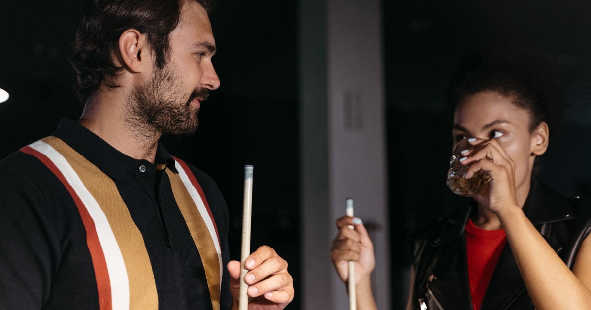 A man and woman socializing over billiards, holding cue sticks and drinks.