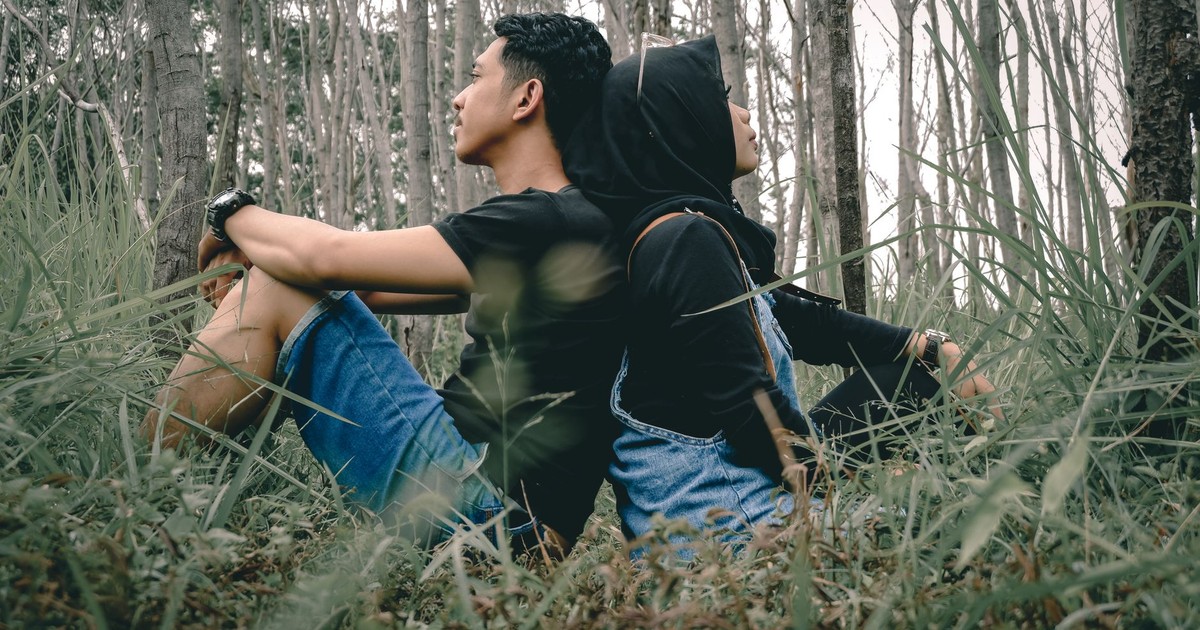 Ground level side view of unrecognizable ethnic man with girlfriend enjoying forest with dry trees on meadow in fall while looking away