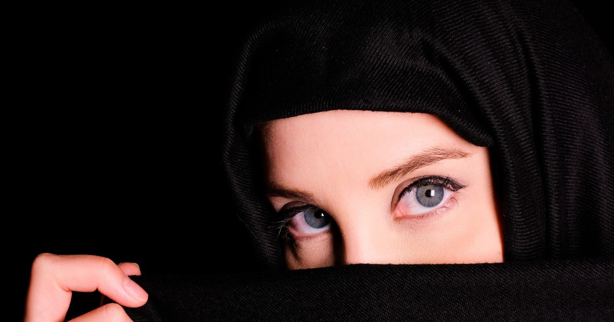 Close-up portrait of a woman wearing a headscarf, revealing only her eyes against a black background.