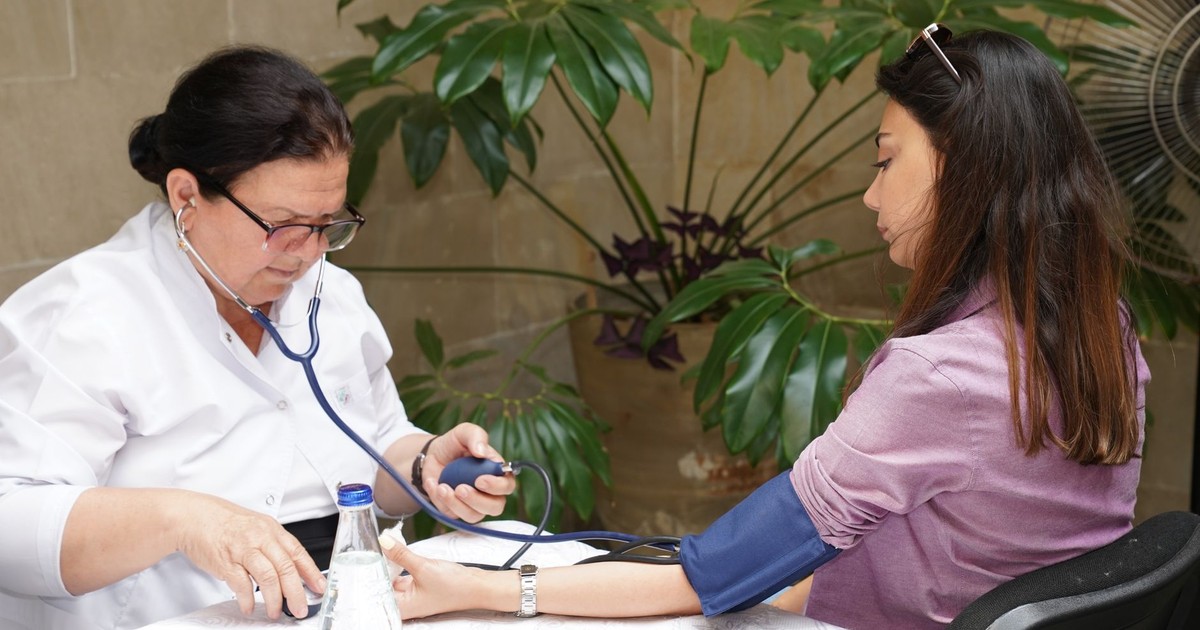 A healthcare worker measures a woman's blood pressure in an outdoor setting, emphasizing wellness and care.