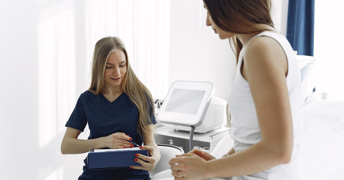 Nurse helping a female patient during a check-up in a modern, bright clinic setting.