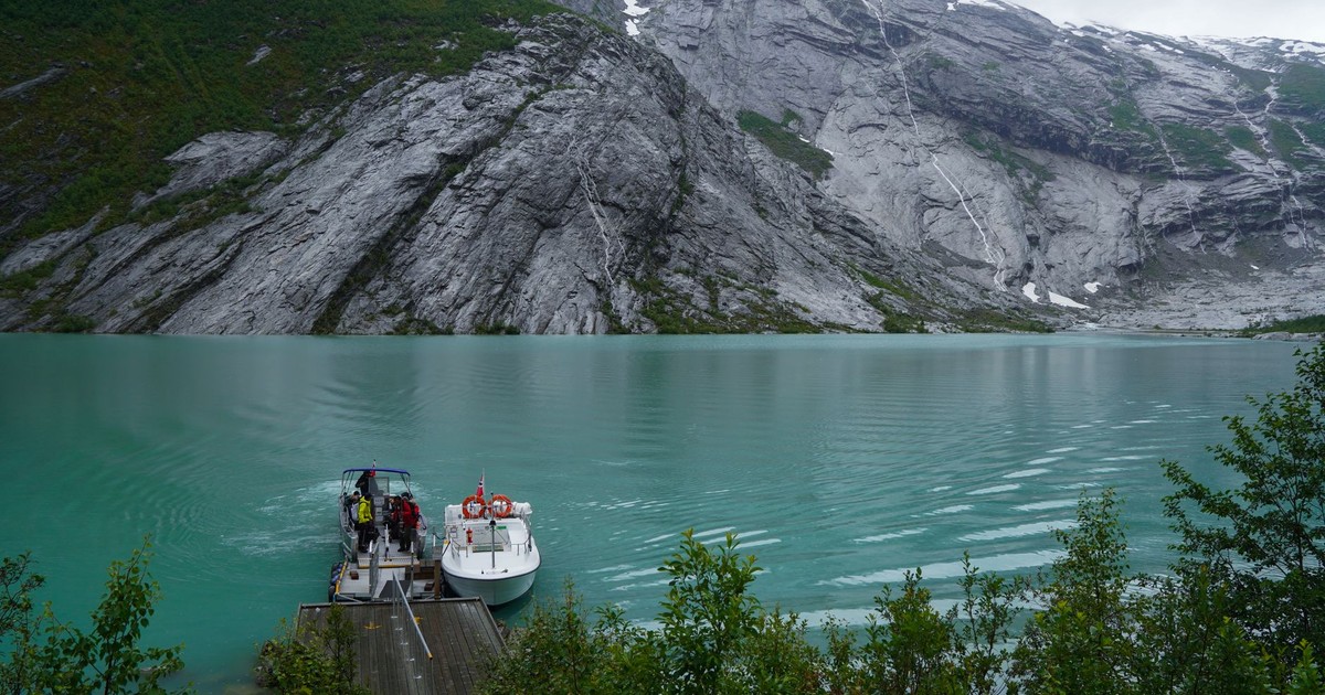 Stunning turquoise water with a boat docked at a fjord surrounded by rugged cliffs in Norway.
