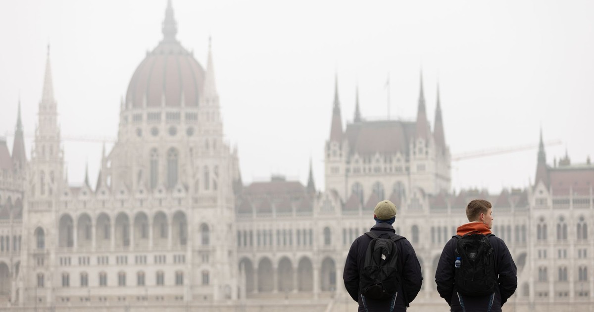 Two tourists with backpacks admire the Hungarian Parliament Building in Budapest on a foggy day.