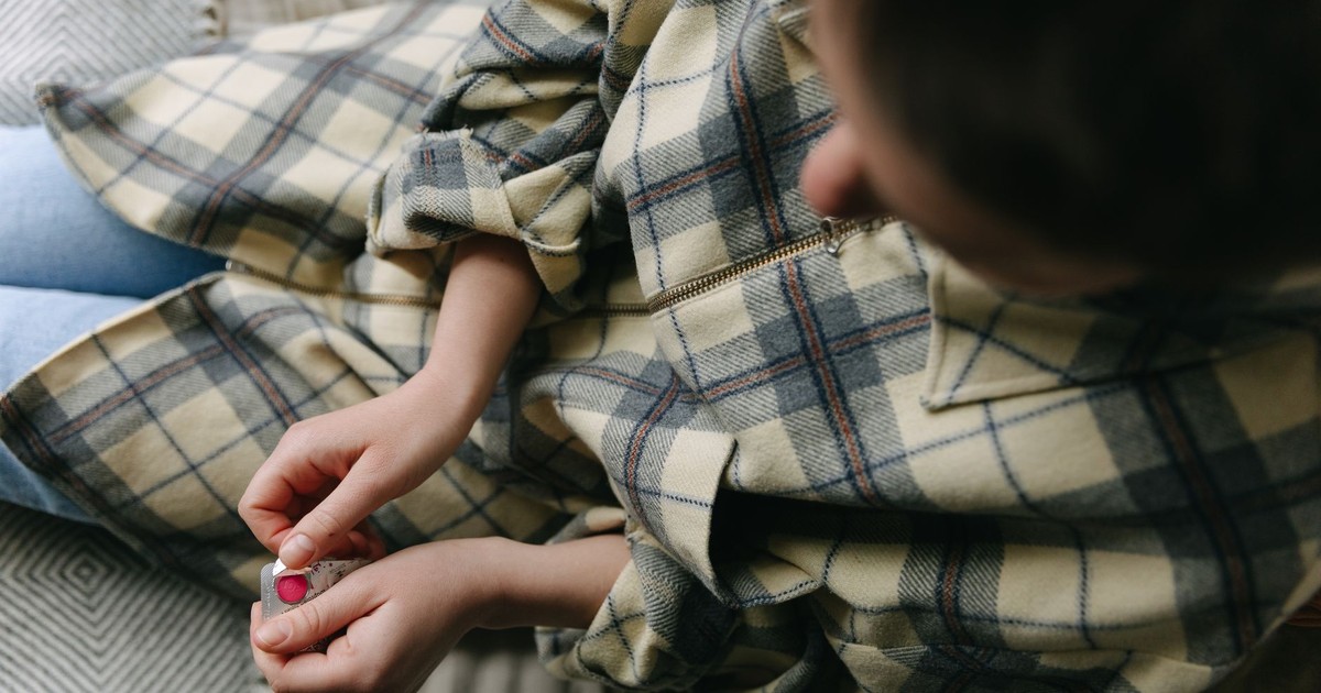 Close-up of hands opening a blister pack while sitting on a sofa with a plaid shirt, indoors.