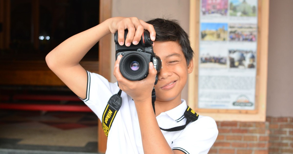 A young boy enthusiastically takes a photo with a DSLR camera indoors.