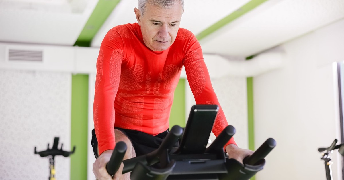 Senior man in red activewear exercising on stationary bike indoors, promoting healthy lifestyle.