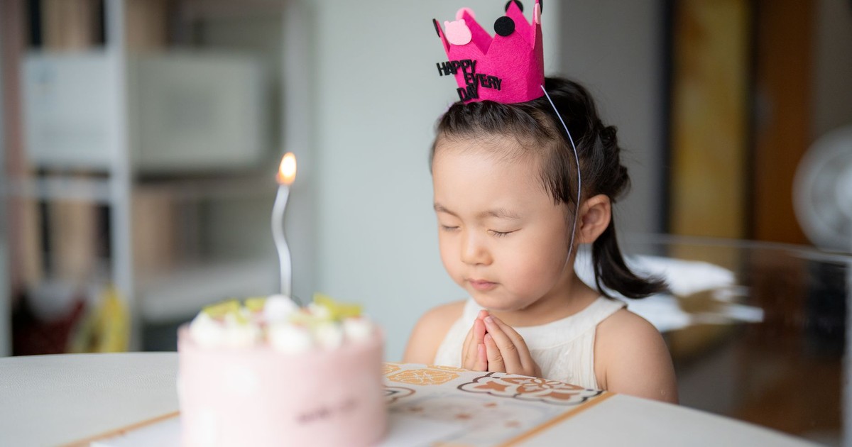 A young girl celebrates her birthday with a delightful pink cake and lit candle, wearing a festive crown.