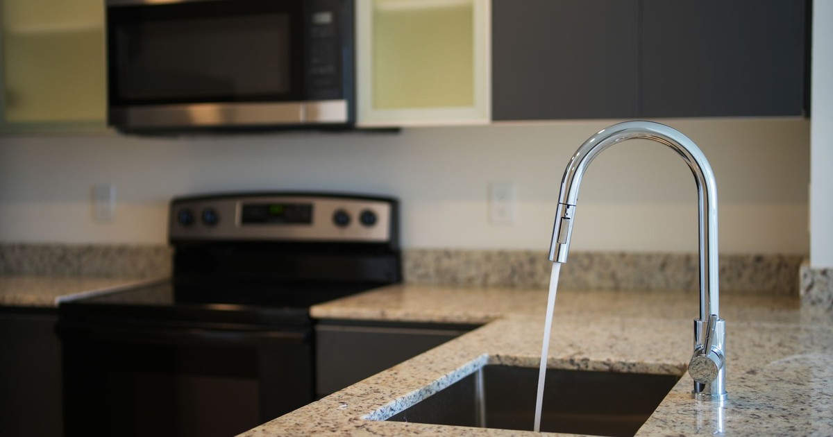 A sleek kitchen faucet on a granite countertop with modern appliances in view.