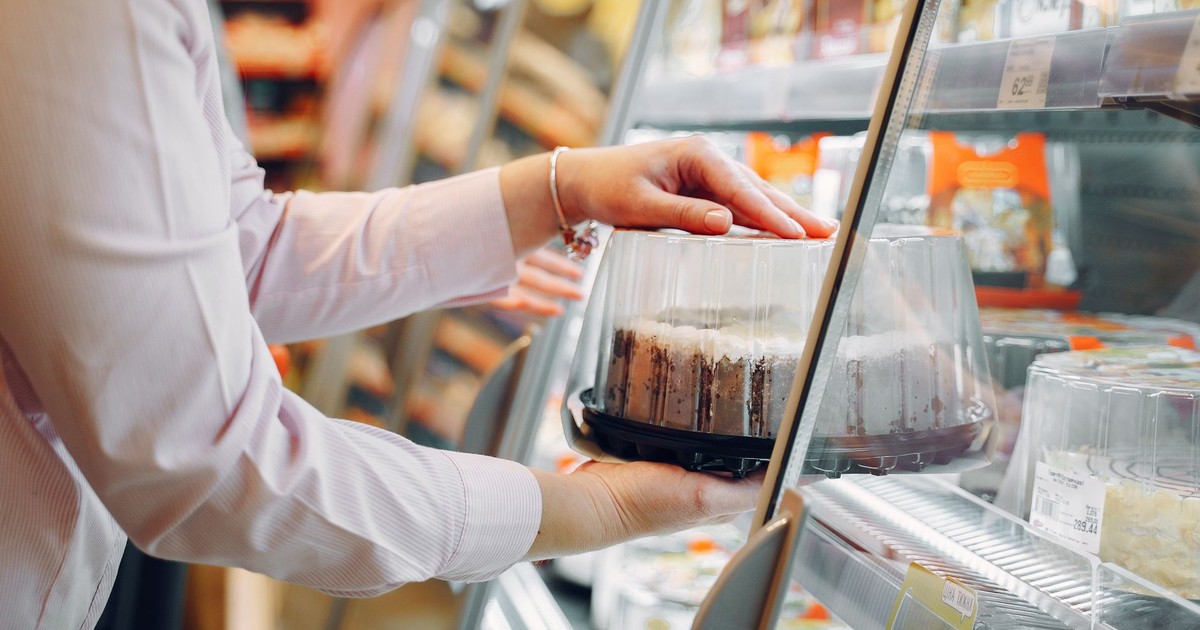 A woman choosing a packaged cake from a supermarket chiller.
