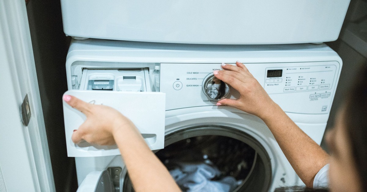 A person in a laundry room adjusting settings on a washing machine.