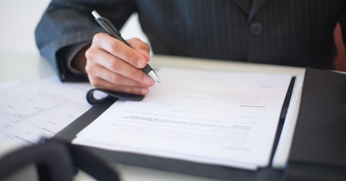 Close-up of a hand signing documents with a pen, symbolizing an important business contract.