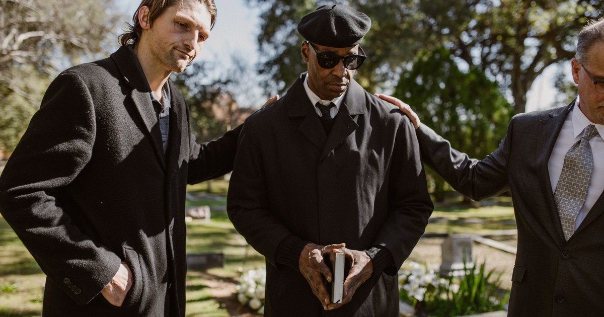 Men in black coats standing together during a somber outdoor funeral service.