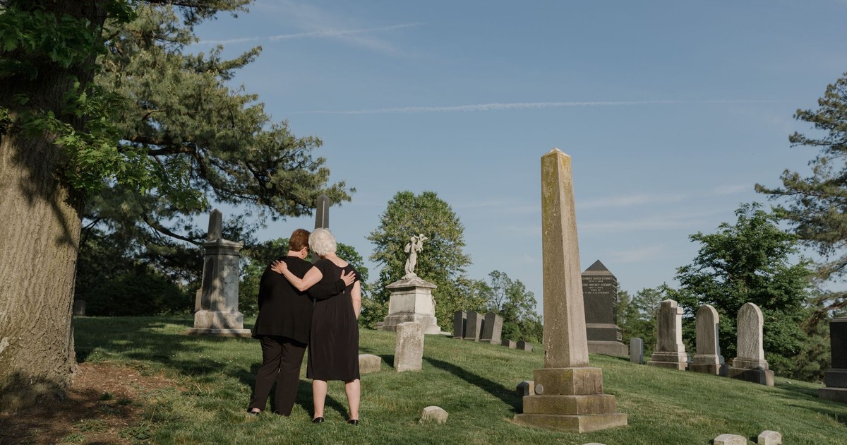 Two adults embracing in a tranquil cemetery, symbolizing love and remembrance.