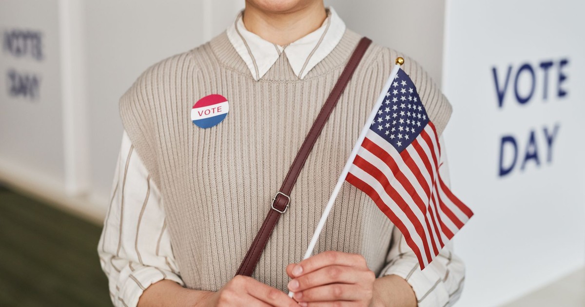 A woman proudly holds the American flag and smiles, celebrating voting day.