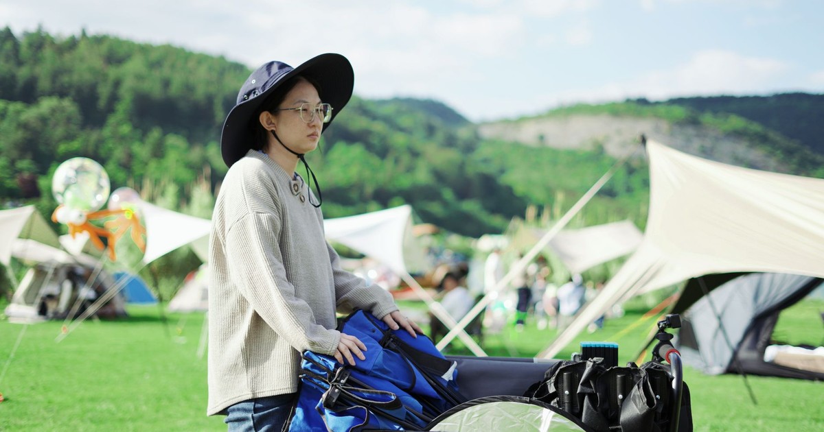 Person preparing camping setup in a scenic outdoor area with tents and lush scenery.