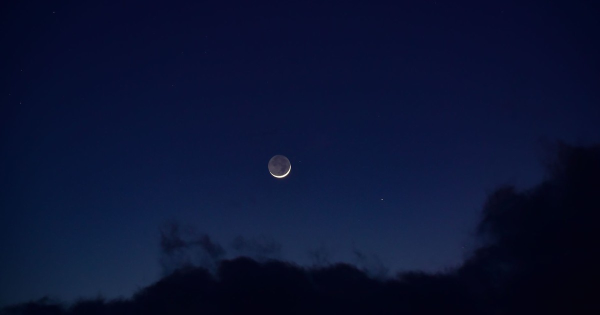 A serene crescent moon surrounded by deep blue night sky and fluffy clouds.