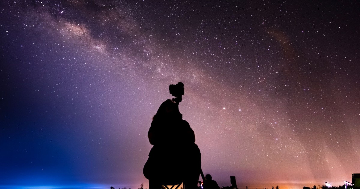 Silhouette of a stargazer with camera capturing the Milky Way under a stunning star-filled night sky.