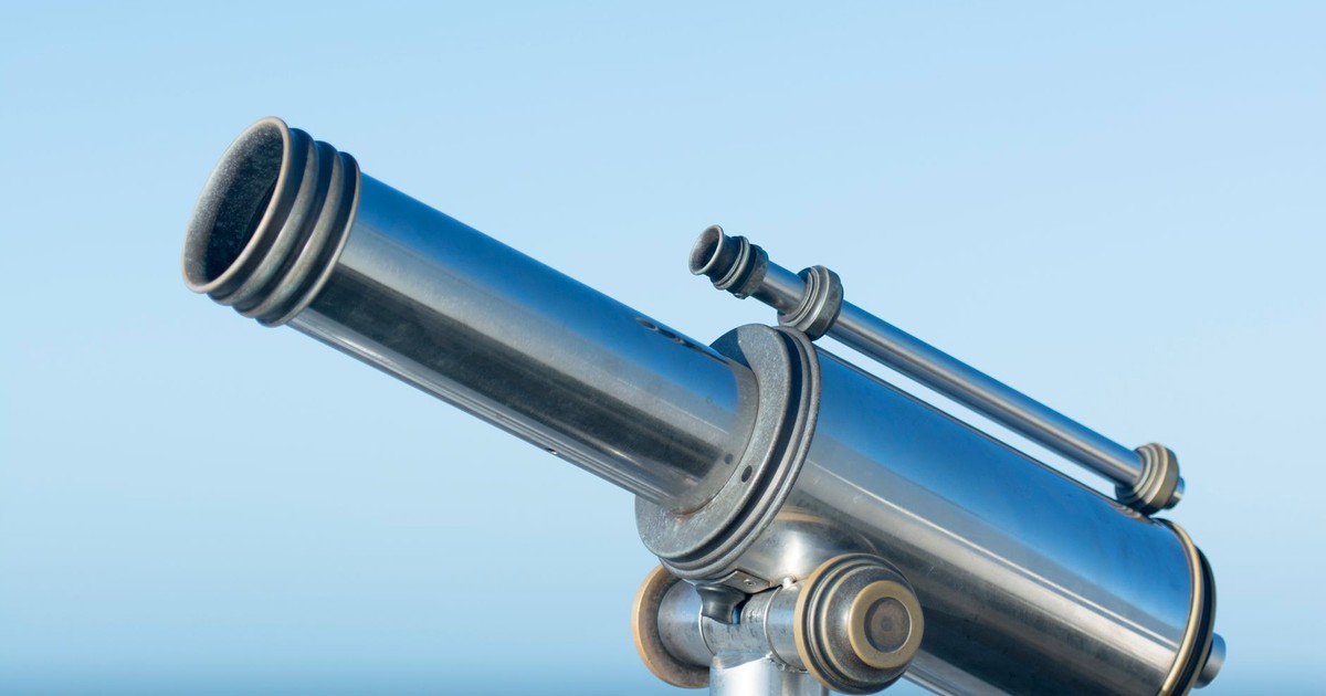 A sleek metallic coin-operated telescope pointing into a clear blue sky, perfect day for sightseeing.