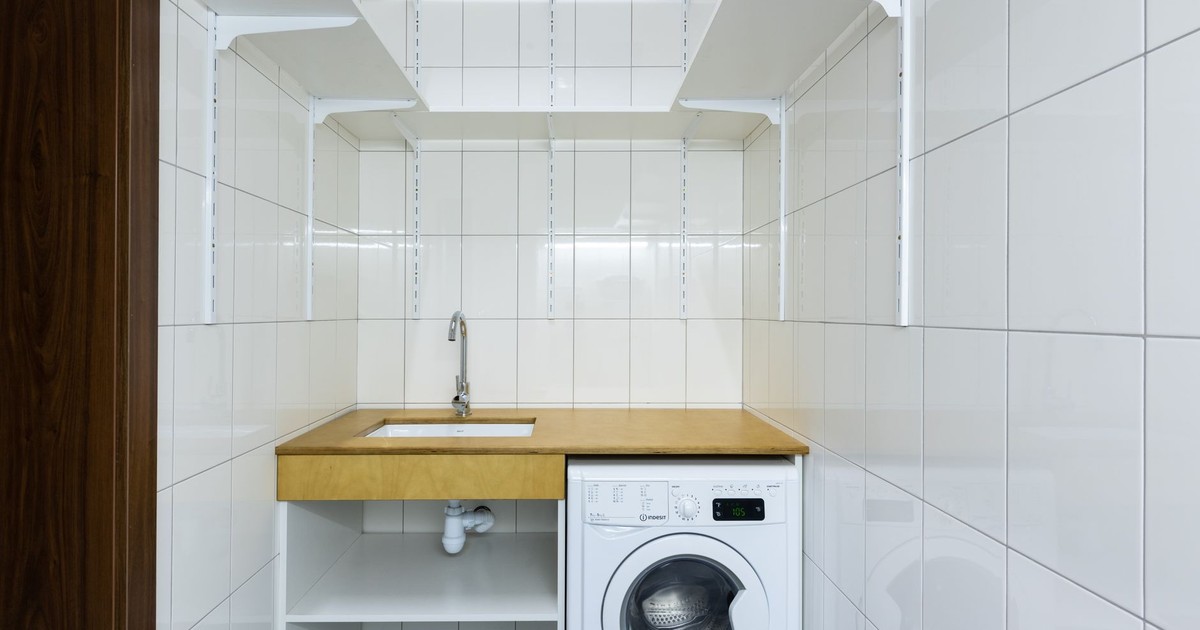 Modern laundry area with white tiled walls, washing machine, and built-in shelves.