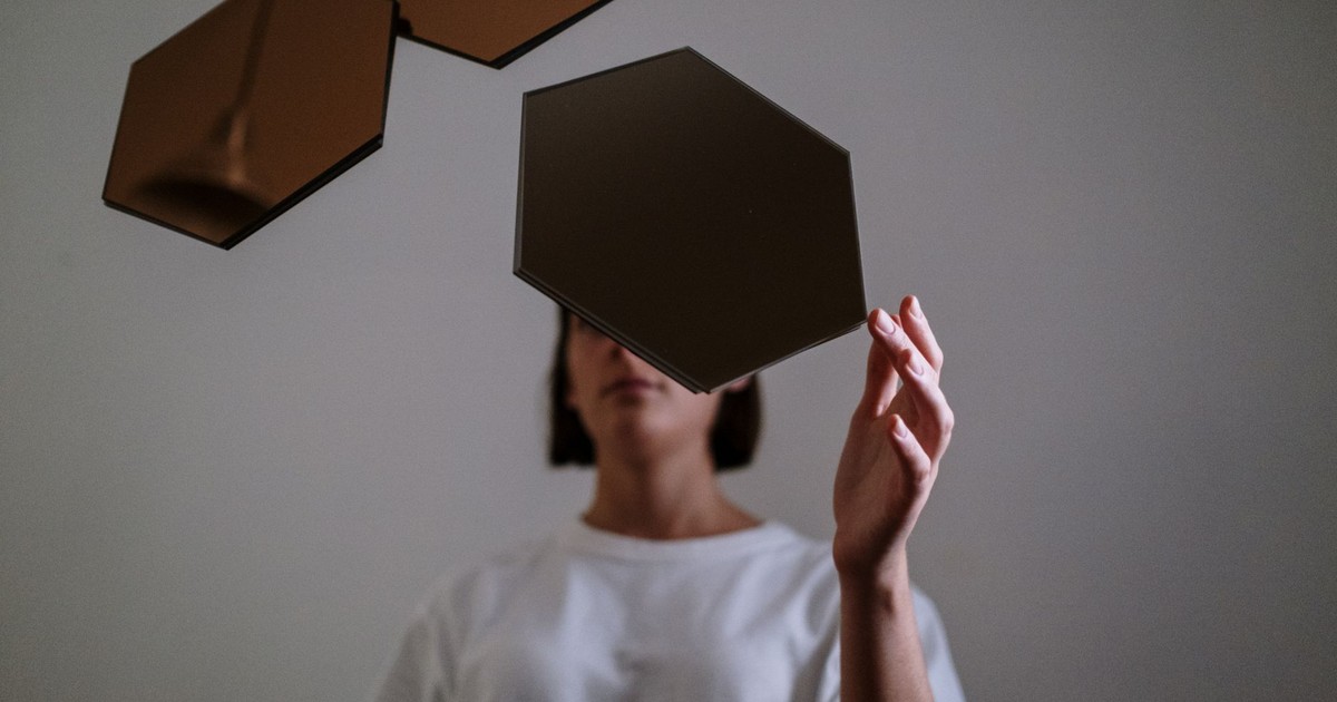 A woman in a white shirt holds geometric mirrors, creating a modern, abstract indoor scene.