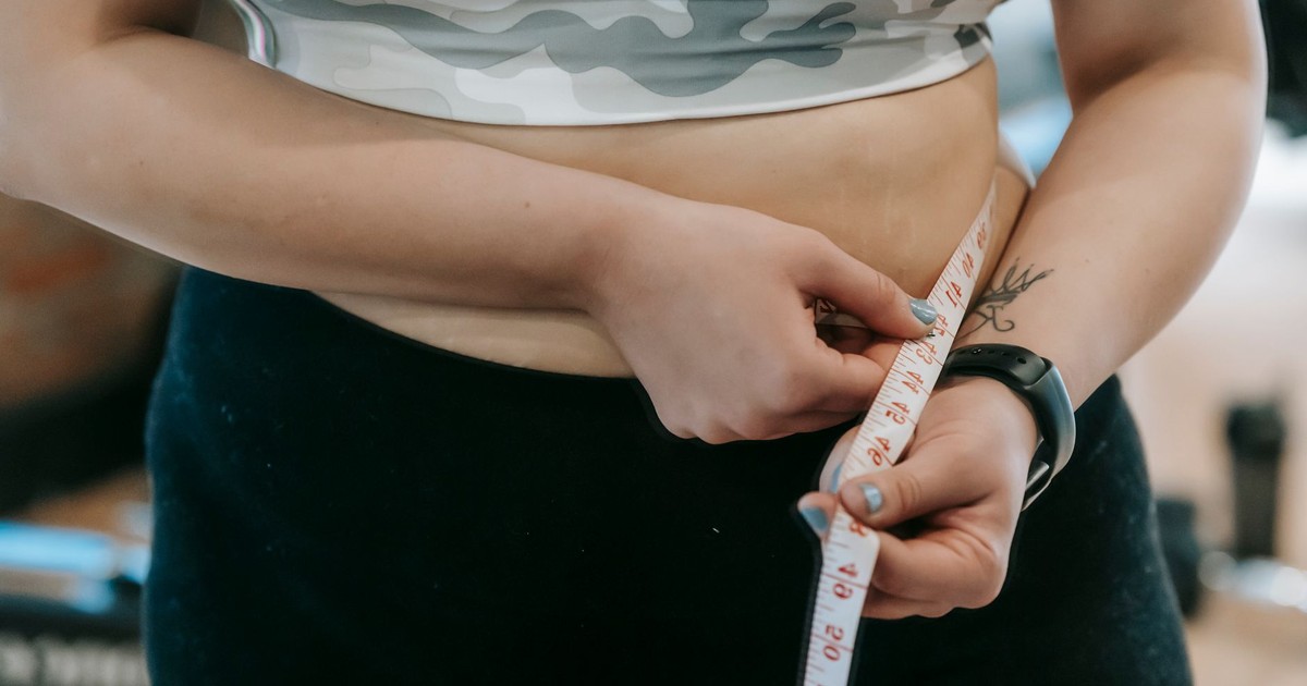 Crop anonymous plus size female with measuring tape measuring waist on blurred background