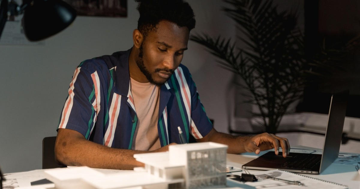 An architect working late at night in an office, using a laptop and surrounded by building models.