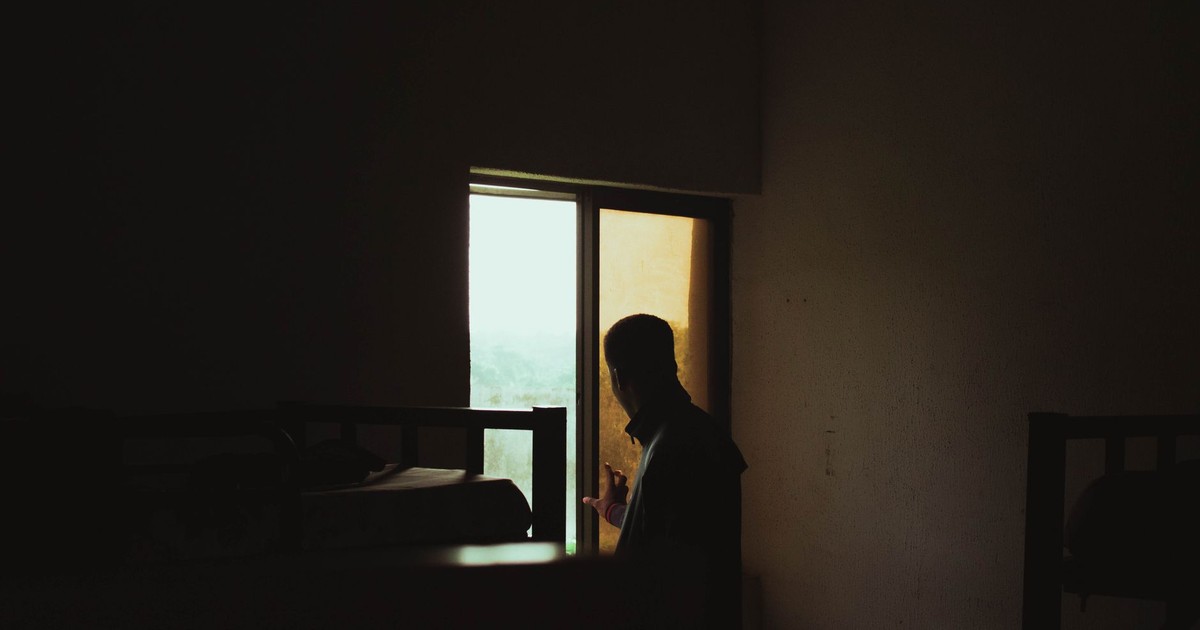 Silhouette of a man gazing out a window in a dimly lit room with bunk beds.