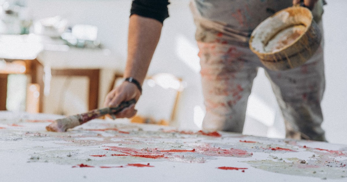 A focused painter applying colorful brushstrokes on a large canvas in a bright studio.