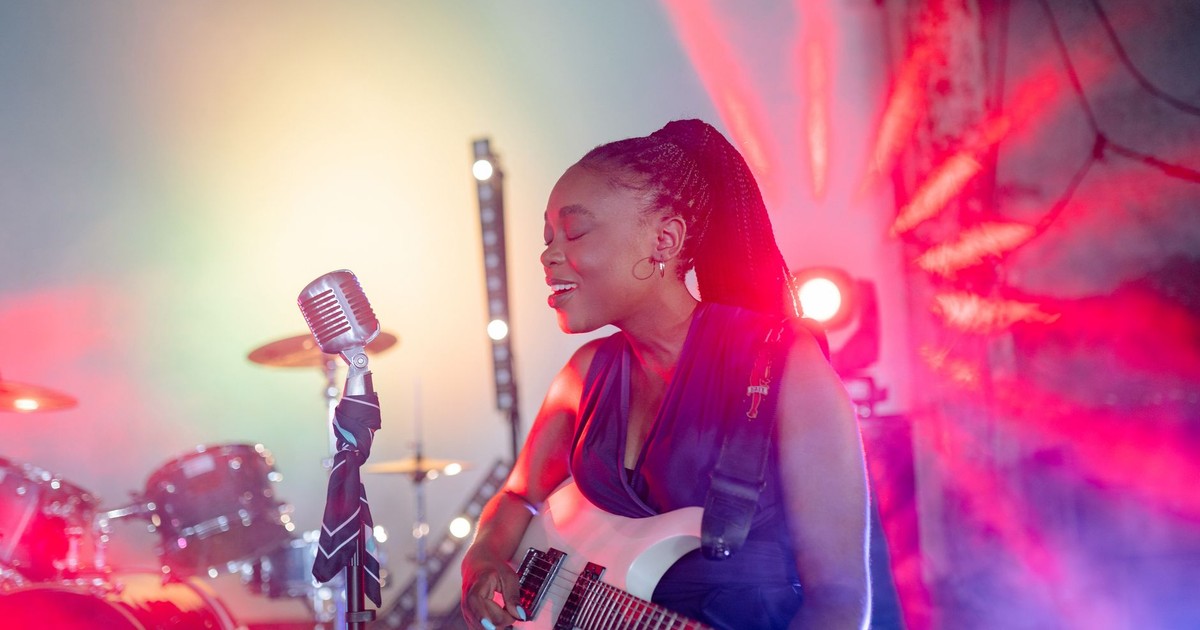Energetic female guitarist performs live with colorful lights and vintage microphone.
