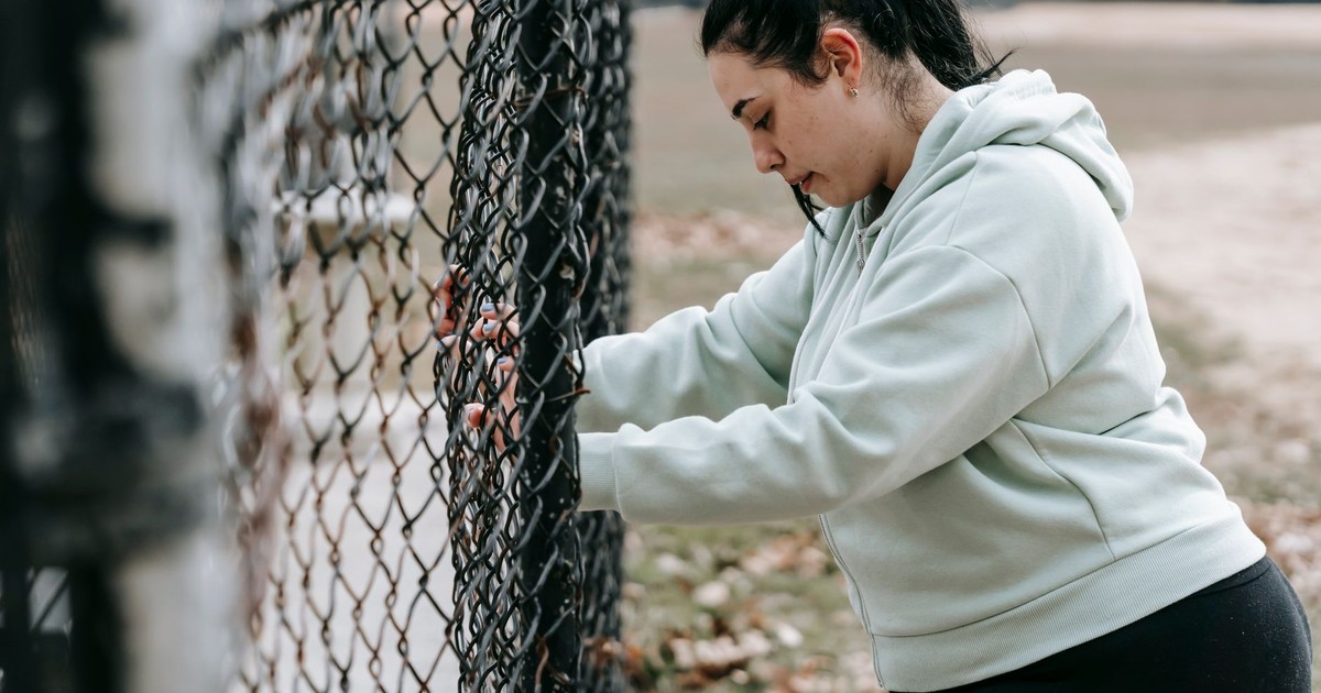 Side view of calm overweight female in sportswear standing near metal fence in park in daytime