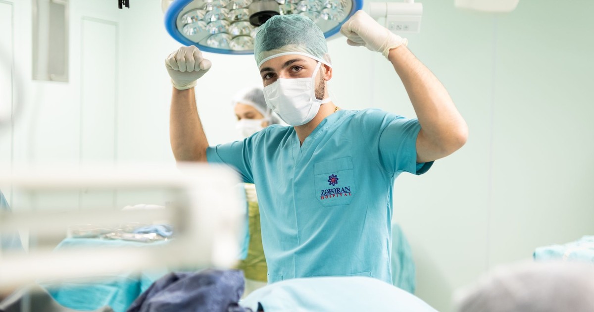 A surgeon in scrubs celebrates after a successful surgery in an operating room.