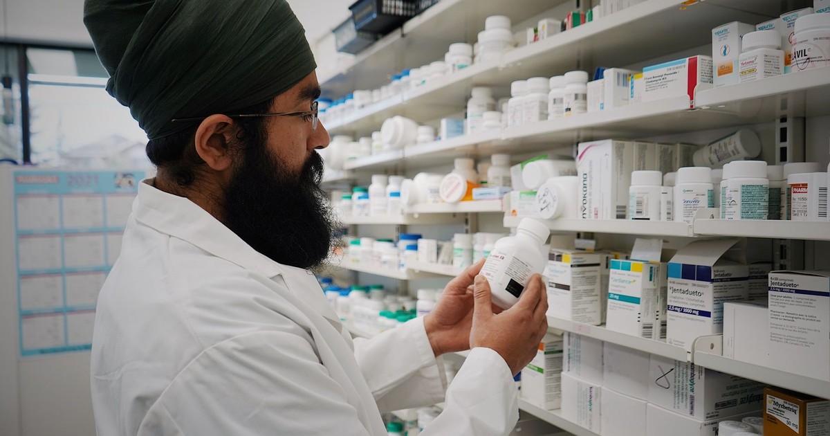 Pharmacist with turban organizing shelves in a pharmacy, focused on healthcare.