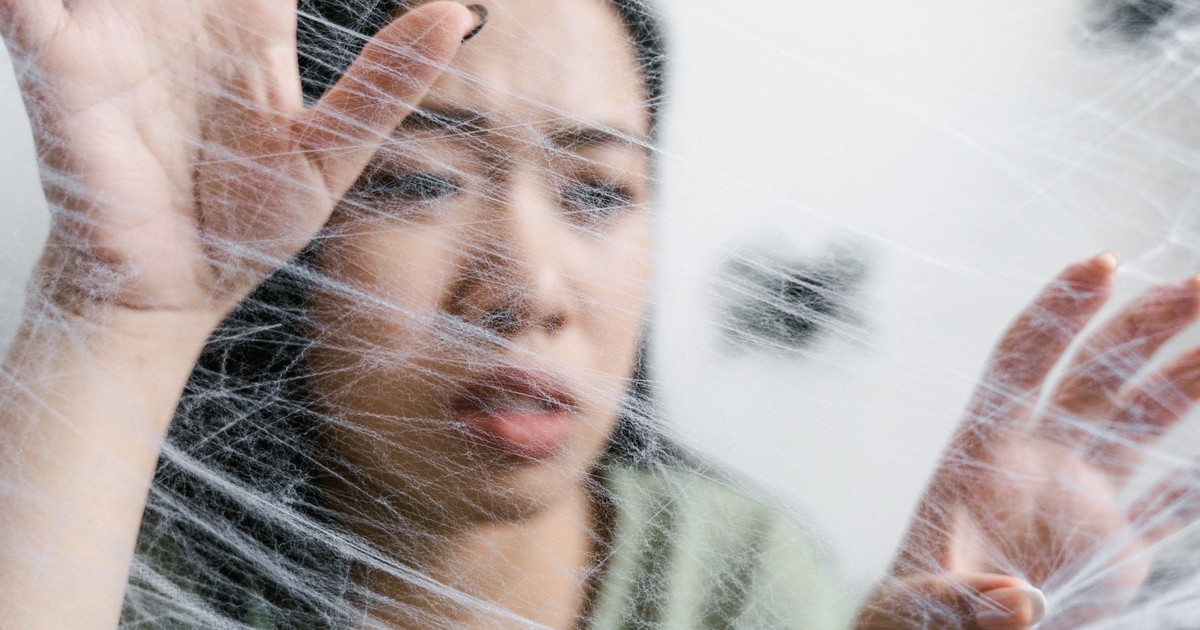 Close-up of a woman looking trapped behind a spider web, conveying anxiety.