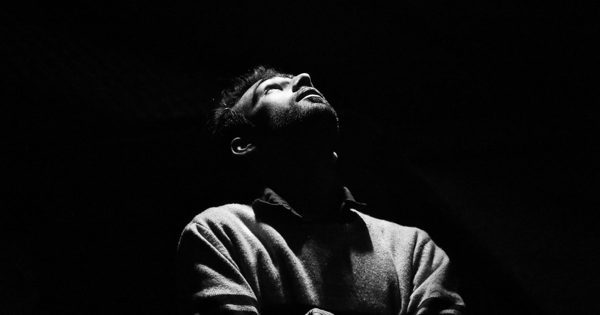 Dramatic black and white portrait of a man looking upwards in low light.