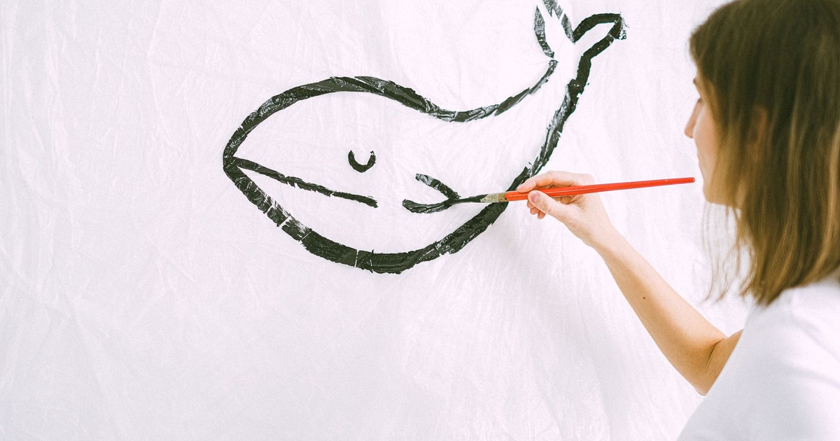 A woman artist painting a minimalist black whale on white canvas indoors.