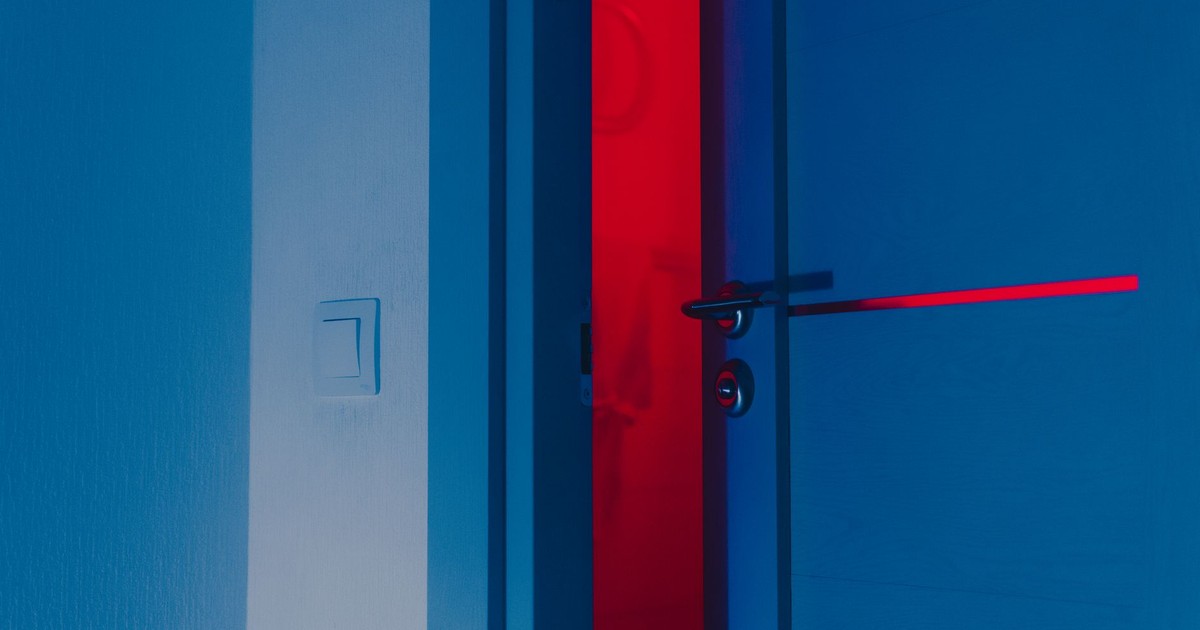 A half-open blue door illuminated by a dramatic red light reveals a unique interior atmosphere.