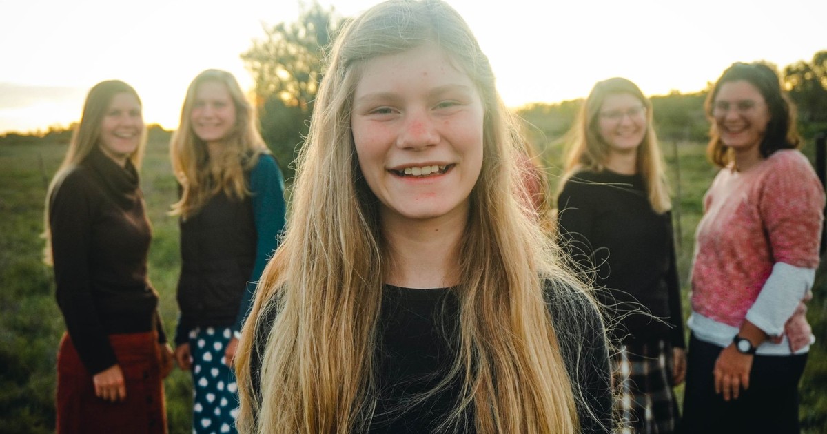 Outdoor group portrait of smiling teenage girl with friends in a field during sunset.