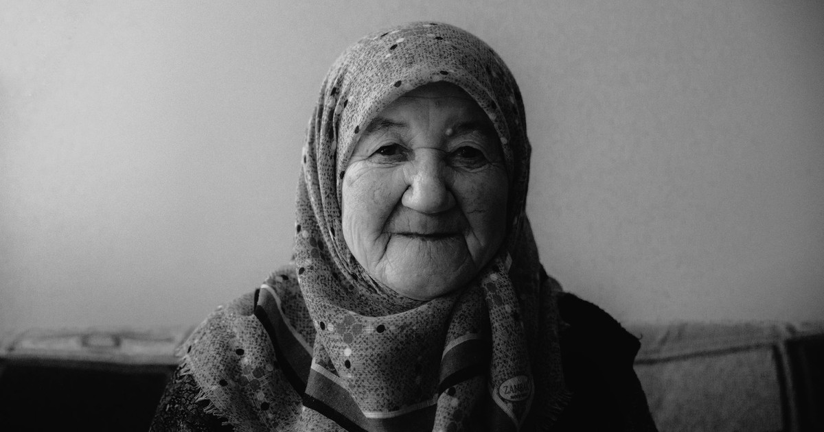 Black and white portrait of an elderly woman smiling warmly, wearing a hijab indoors.